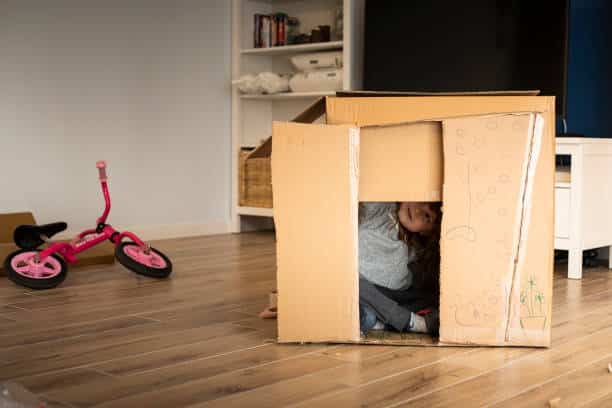 Little child girl playing in a cardboard playhouse while moving in a new house.